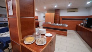 A buffet area with various food items, a counter with plates, and a kitchen in the background. - Qawra Point Holiday Complex (St. Paul's Bay)
