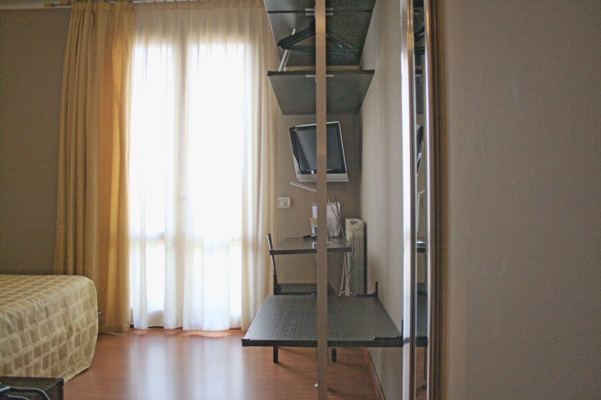 A hotel room with a bed, a desk with a computer, and a window with curtains.