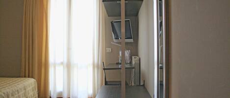 A hotel room with a bed, a desk with a computer, and a window with curtains.