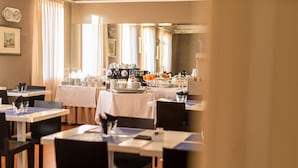 Un comedor de hotel con mesas dispuestas para el desayuno, incluyendo cafeteras y fruta.