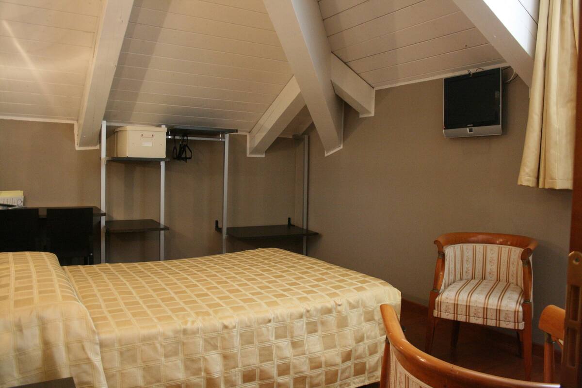 A bedroom with a bed, a chair, a desk, and a TV mounted on the wall.
