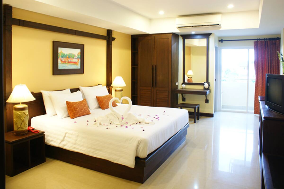 A hotel room with a large bed, two bedside tables with lamps, a wardrobe, a mirror, and a television.