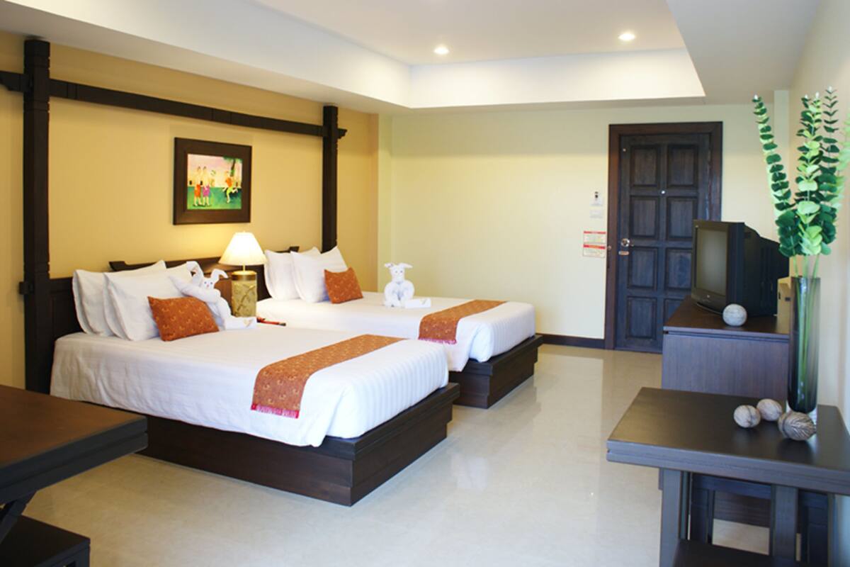 A hotel room with two beds, a desk, a TV, and a plant.