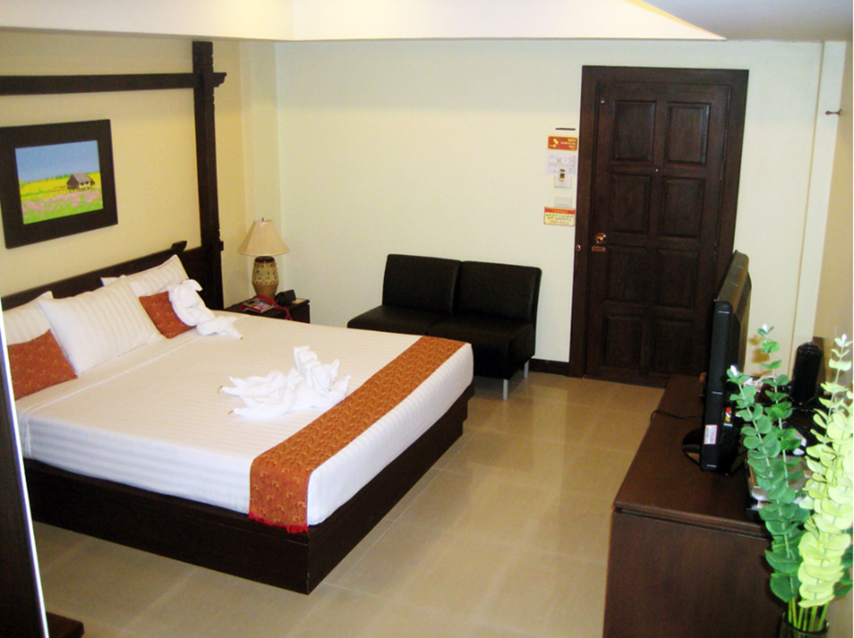 A hotel room with a bed, a sofa, a television, and a door.