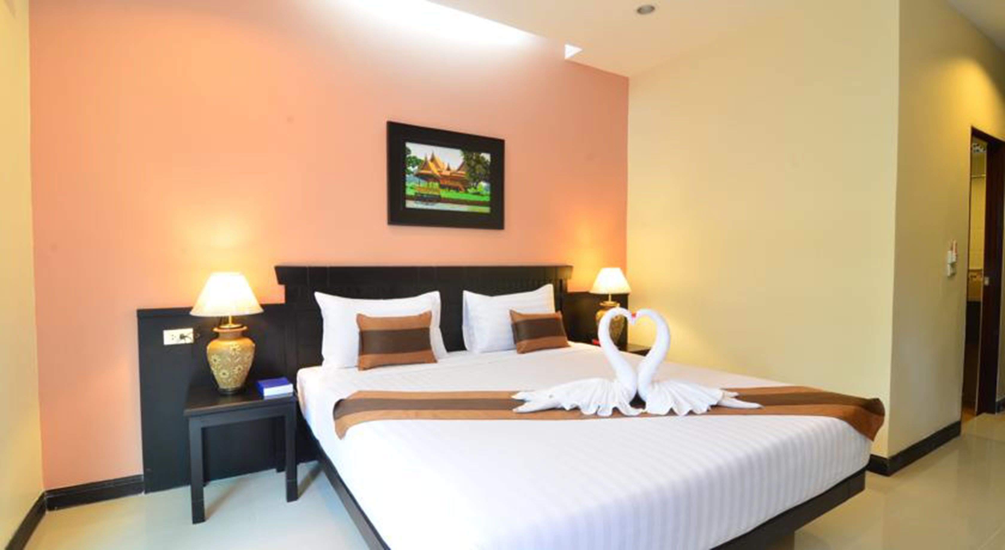 A hotel room with a large bed, two bedside lamps, a framed picture on the wall, and a swan-shaped decoration on the bed.