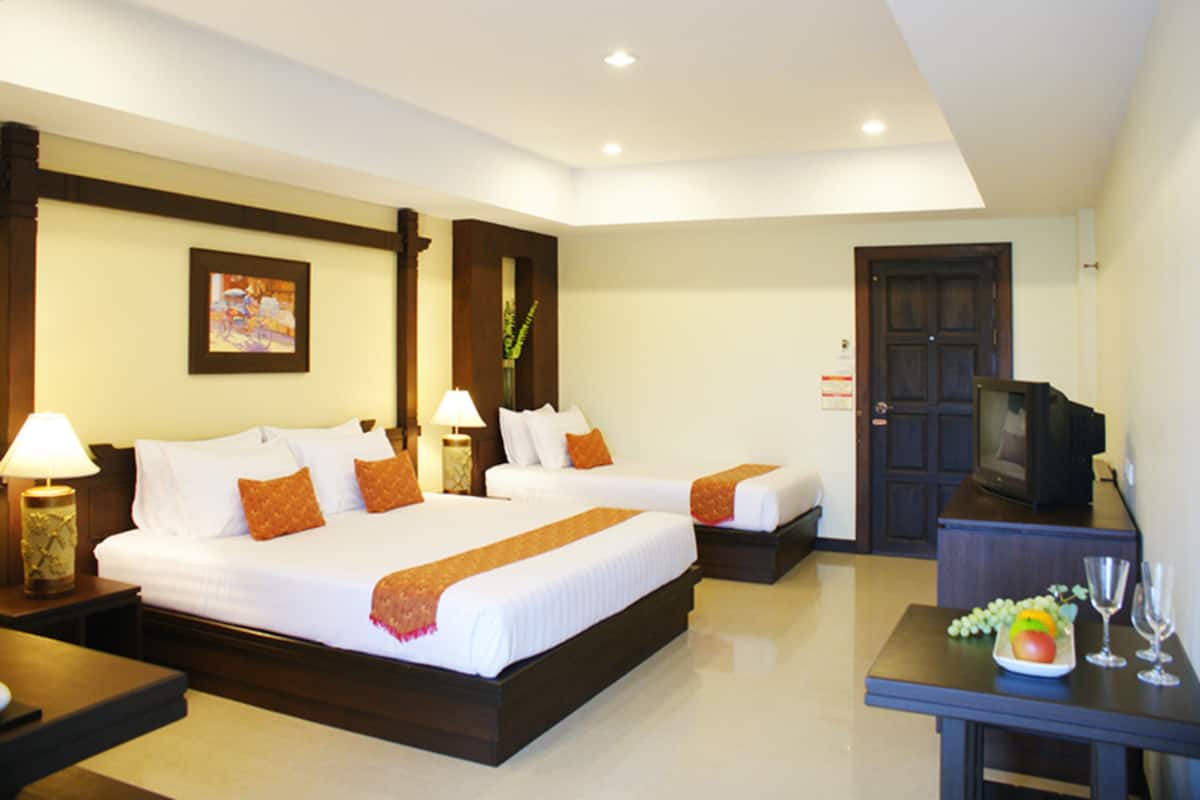 A hotel room with two beds, a TV, a small table with fruit and glasses, and a door.