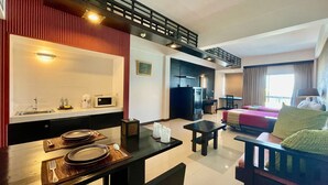 A hotel room with a kitchenette, a dining area, a living area with a sofa and a TV, and a balcony with a railing. - Siam Piman Hotel (Bangkok)
