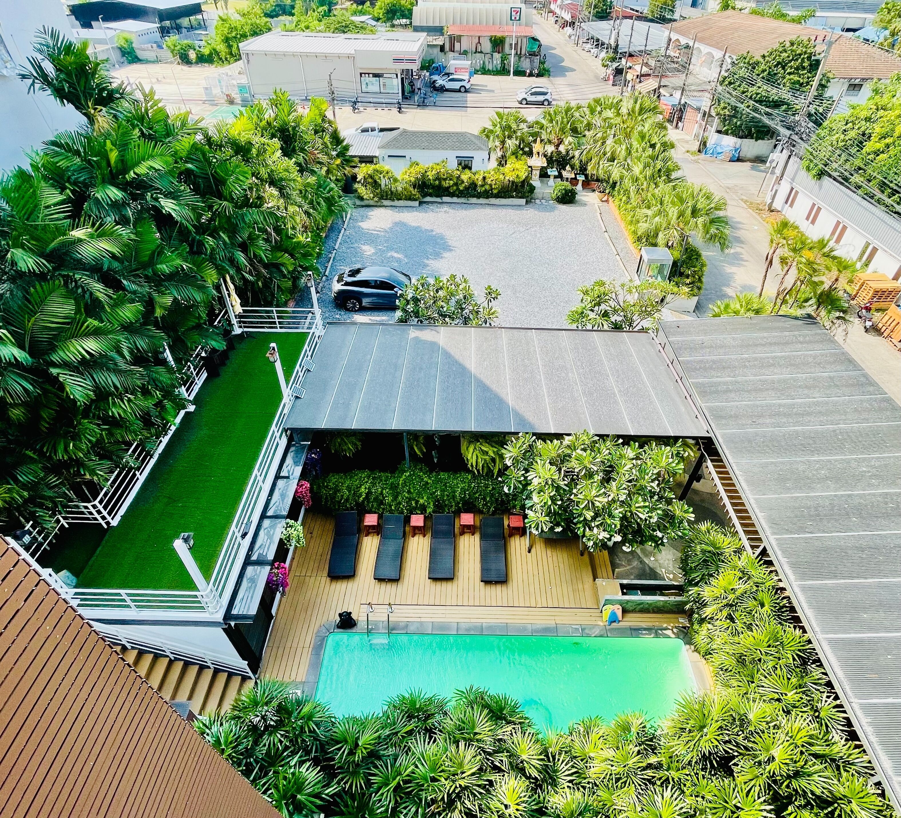 An aerial view of a residential property with a swimming pool, a deck with sun loungers, and a fenced garden area.