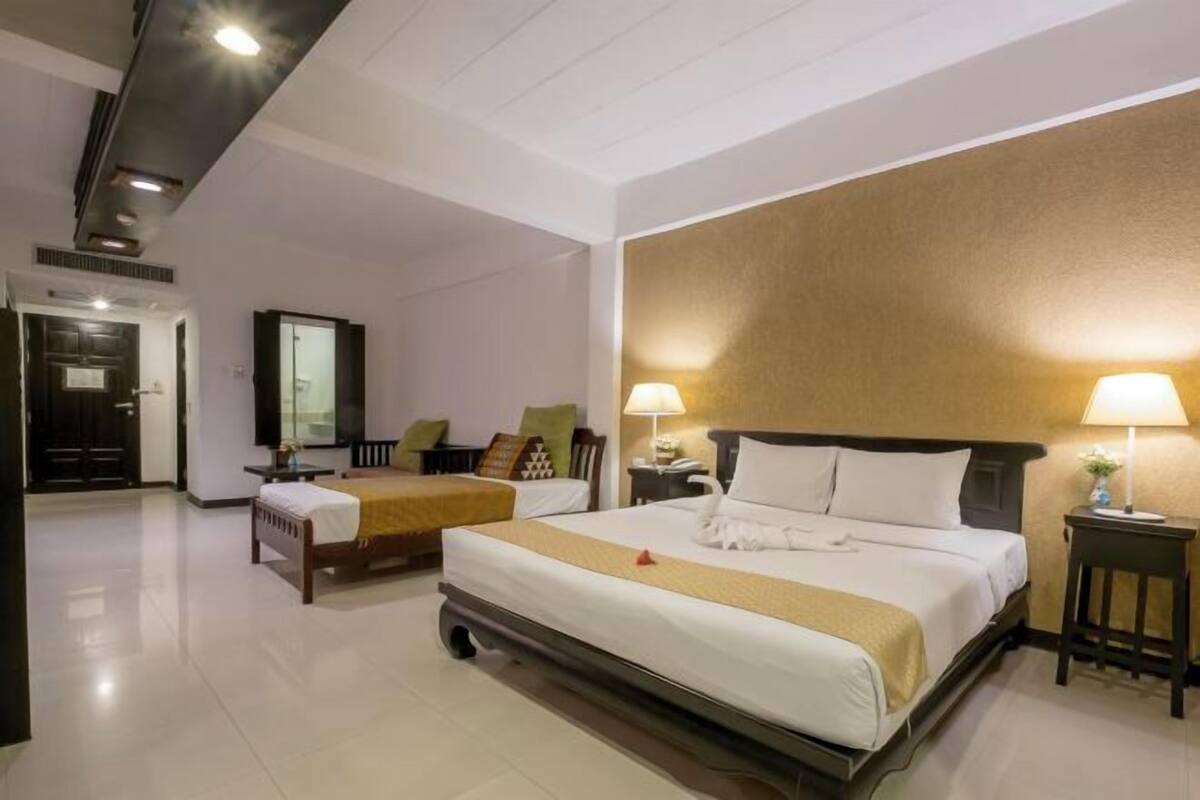 Een hotelkamer met een groot bed, een kleiner bed, een bureau, een stoel, een lamp en een spiegel.