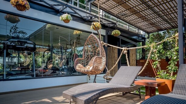 A modern outdoor lounge area with wicker furniture, a hanging chair, and potted plants. - Siam Piman Hotel (Bangkok)