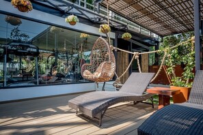 A modern outdoor lounge area with wicker furniture, a hanging chair, and potted plants. - Siam Piman Hotel (Bangkok)