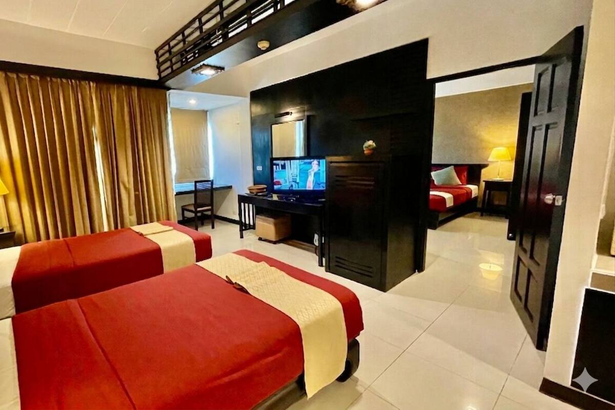 Een hotelkamer met twee bedden, een bureau, een televisie en een deur naar een andere kamer.