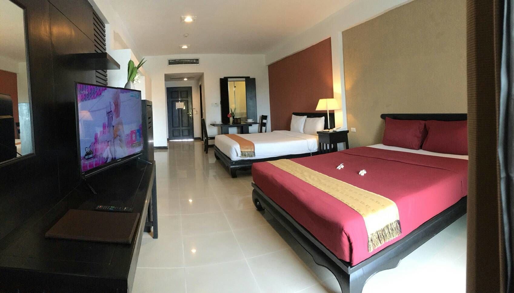 A hotel room with a TV, two beds, a desk, and a mirror.