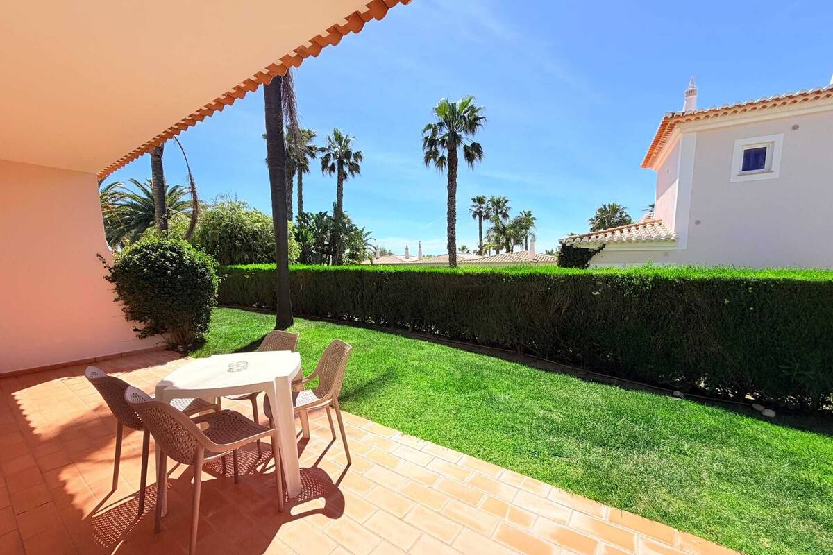 A patio with a table and chairs, a well-maintained lawn, and a white building in the background.