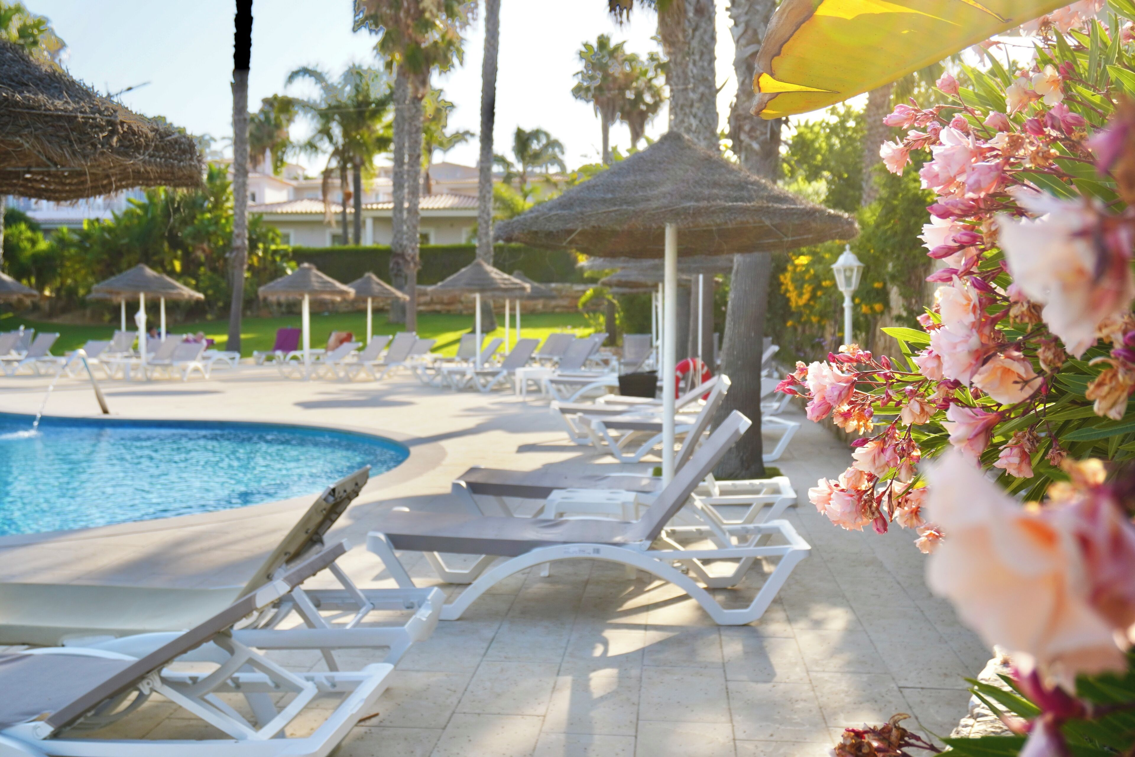 Zona junto a la piscina con sillones de descanso y sombrillas de paja.