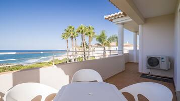 Un balcone con vista sull'oceano, sedie bianche e un condizionatore.