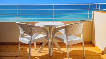 A balcony with two white wicker chairs and a small round table, overlooking a clear blue sea.