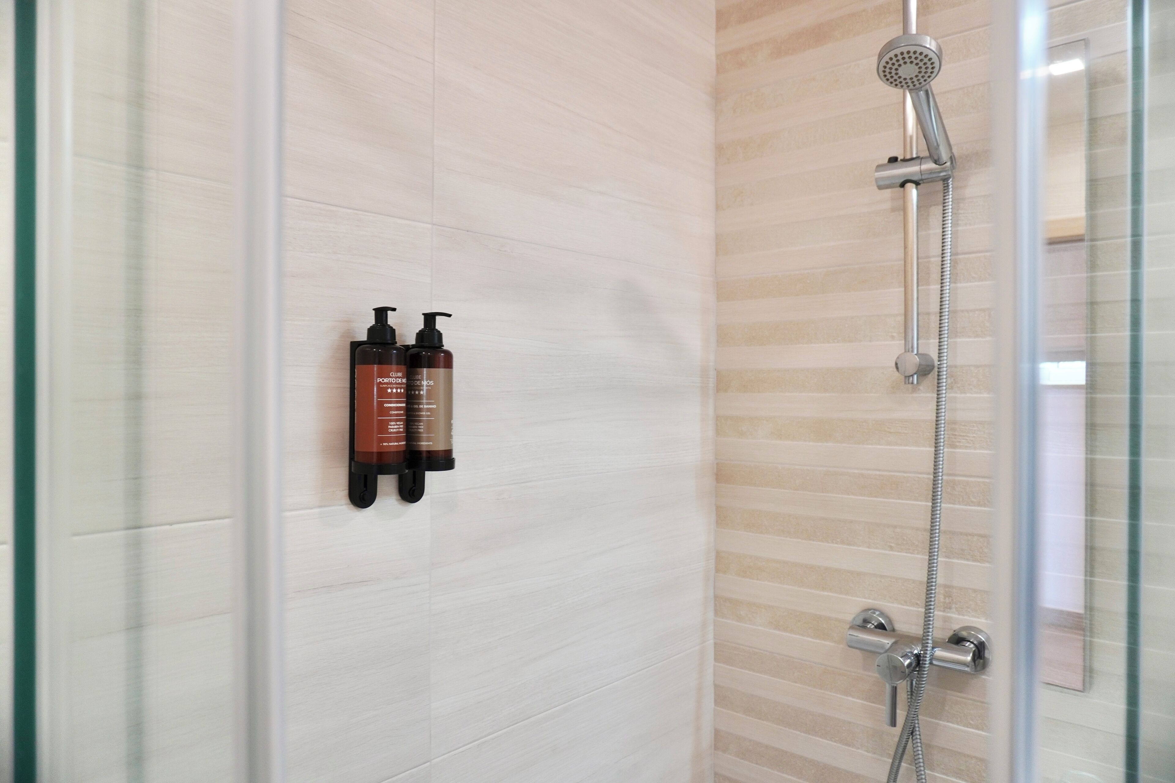 A modern bathroom with a glass shower enclosure, a handheld showerhead, and two bottles of shampoo on the wall.
