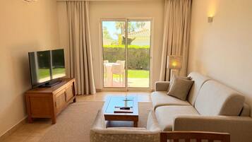 Una sala de estar con televisor, sofá, mesa de centro y vistas al exterior por un ventanal corredero.