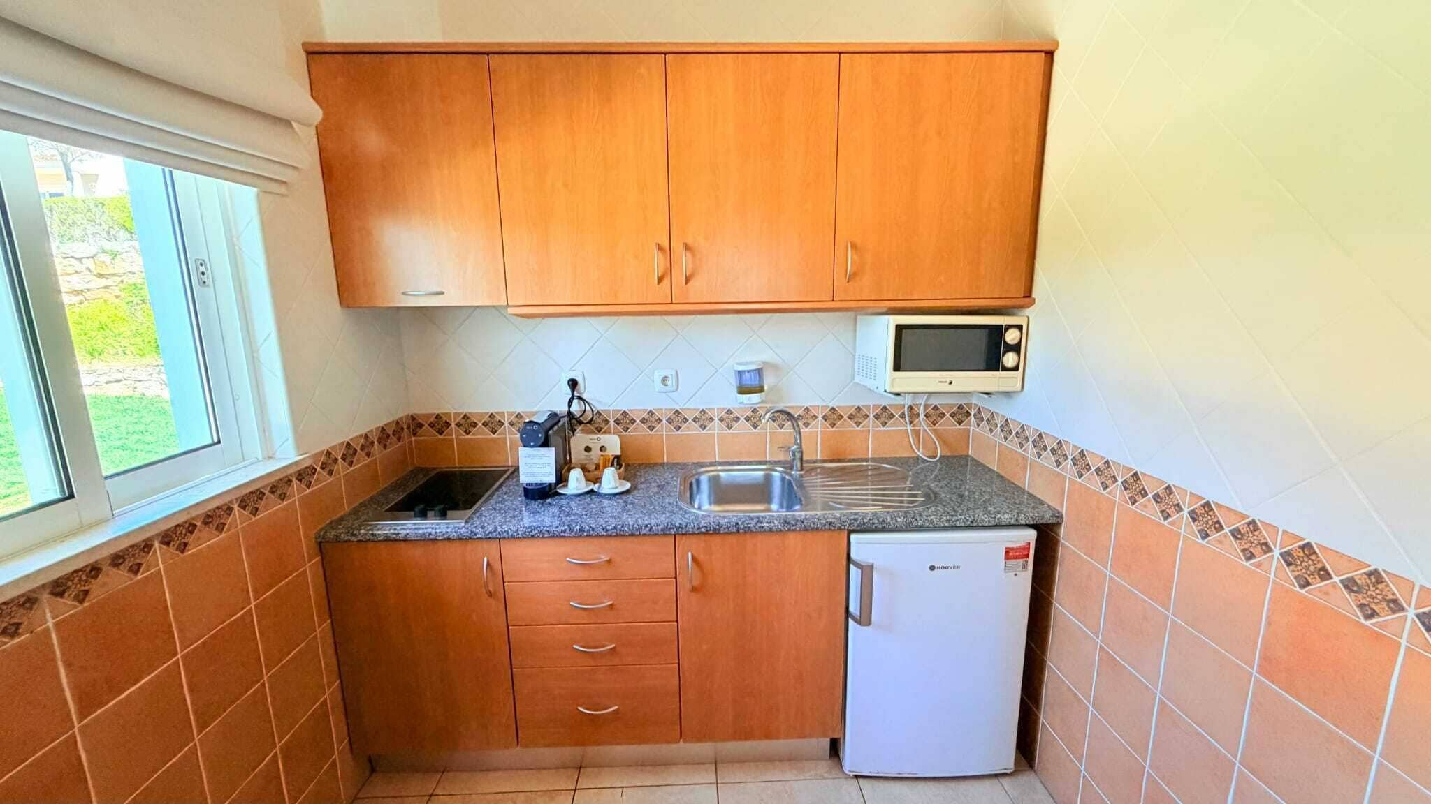 A compact kitchen with wooden cabinets, a microwave, a sink, and a small refrigerator.