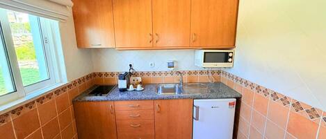 A compact kitchen with wooden cabinets, a microwave, a sink, and a small refrigerator.