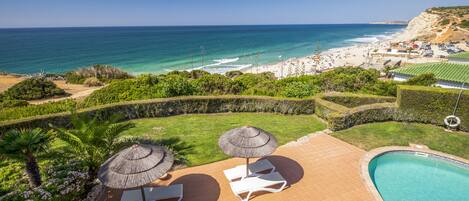 A pool area with lounge chairs and umbrellas, a landscaped garden, and a view of the beach and ocean.