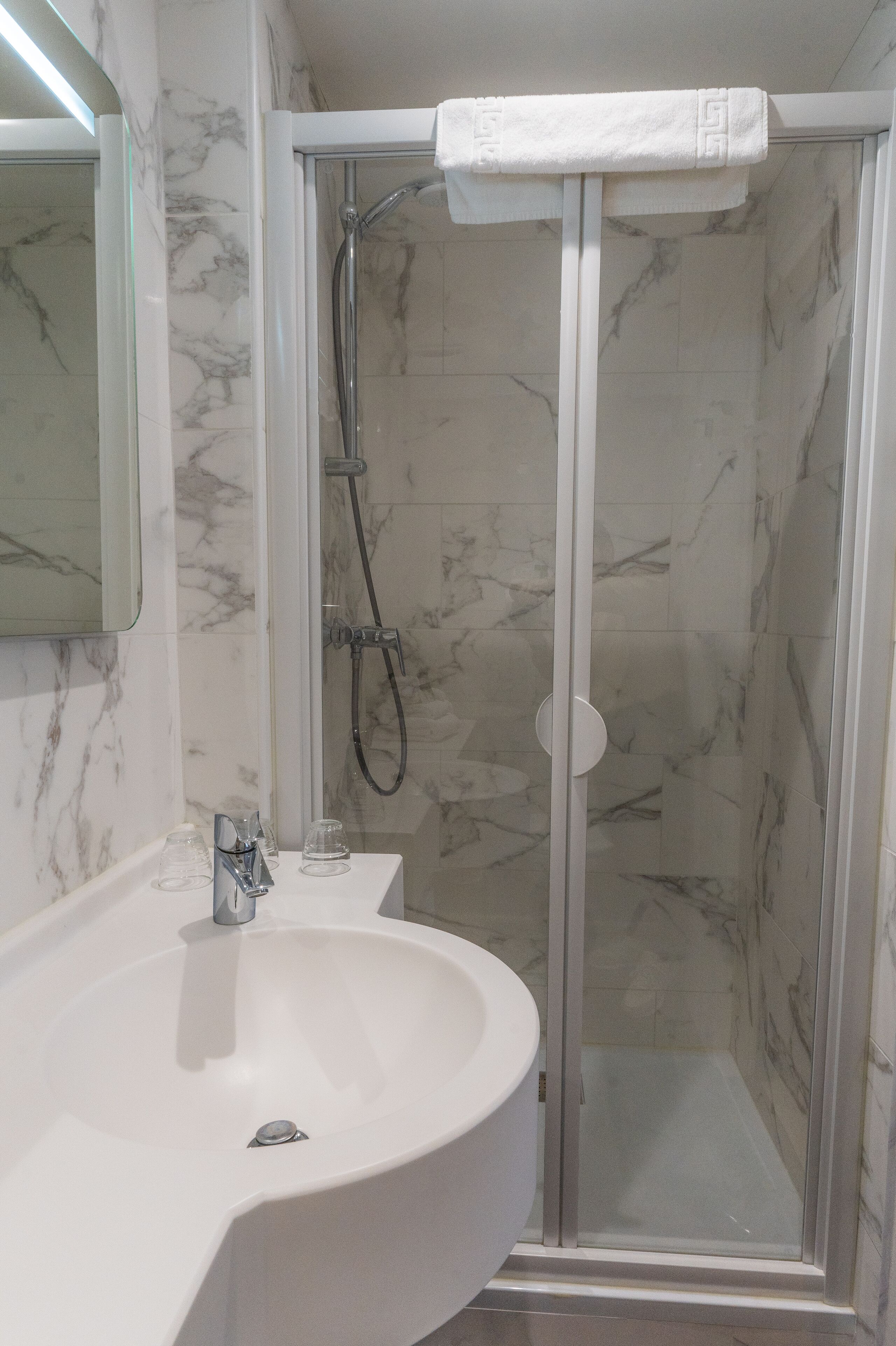 A bathroom with a white sink, a glass shower enclosure, and marble walls.