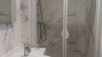 A bathroom with a white sink, a glass shower enclosure, and marble walls.