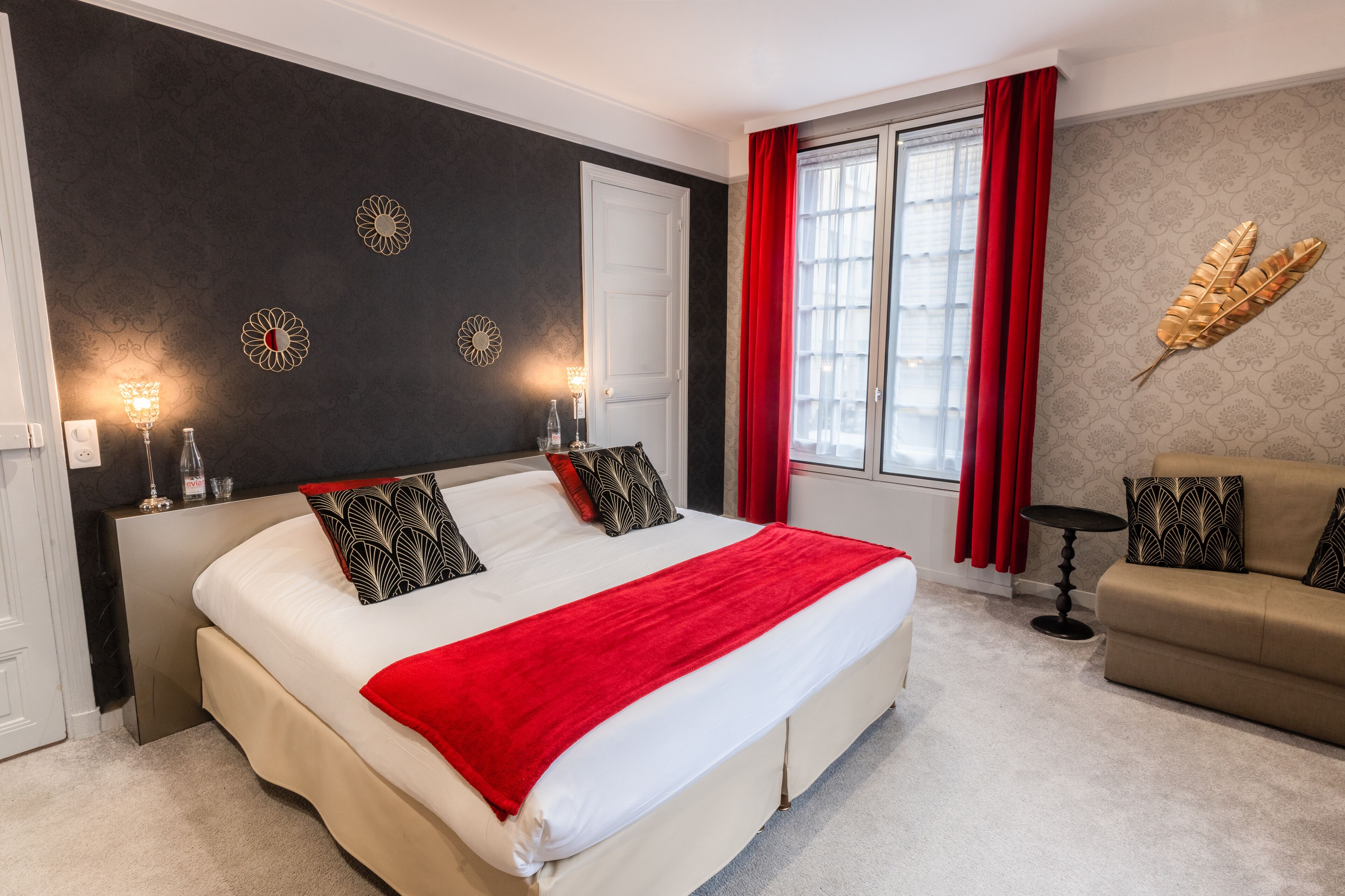 Een slaapkamer met een groot bed, een bank en een raam met rode gordijnen.