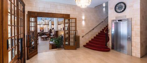 A spacious lobby with a grand chandelier, a staircase, and an elevator.