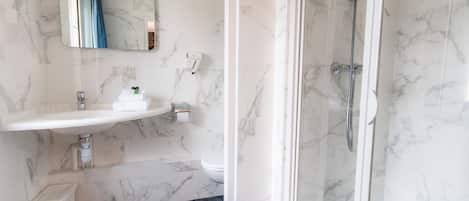 Un baño con lavamanos de mármol, inodoro y ducha con mampara de vidrio.