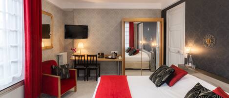 Una habitación de hotel con cama, escritorio, silla, televisión y espejo.