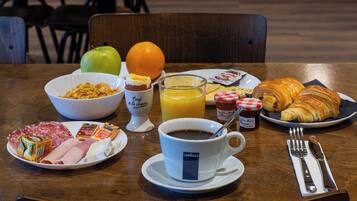 A breakfast table with croissants, orange juice, coffee, and a bowl of cereal.