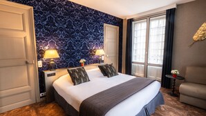 Een hotelkamer met een groot bed, twee bedlampen, een tafeltje met een plant en een bank.