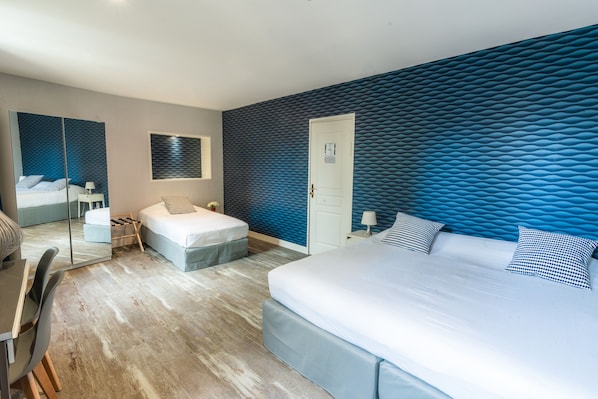 A modern hotel room with a large bed, a desk, a chair, and a mirror.