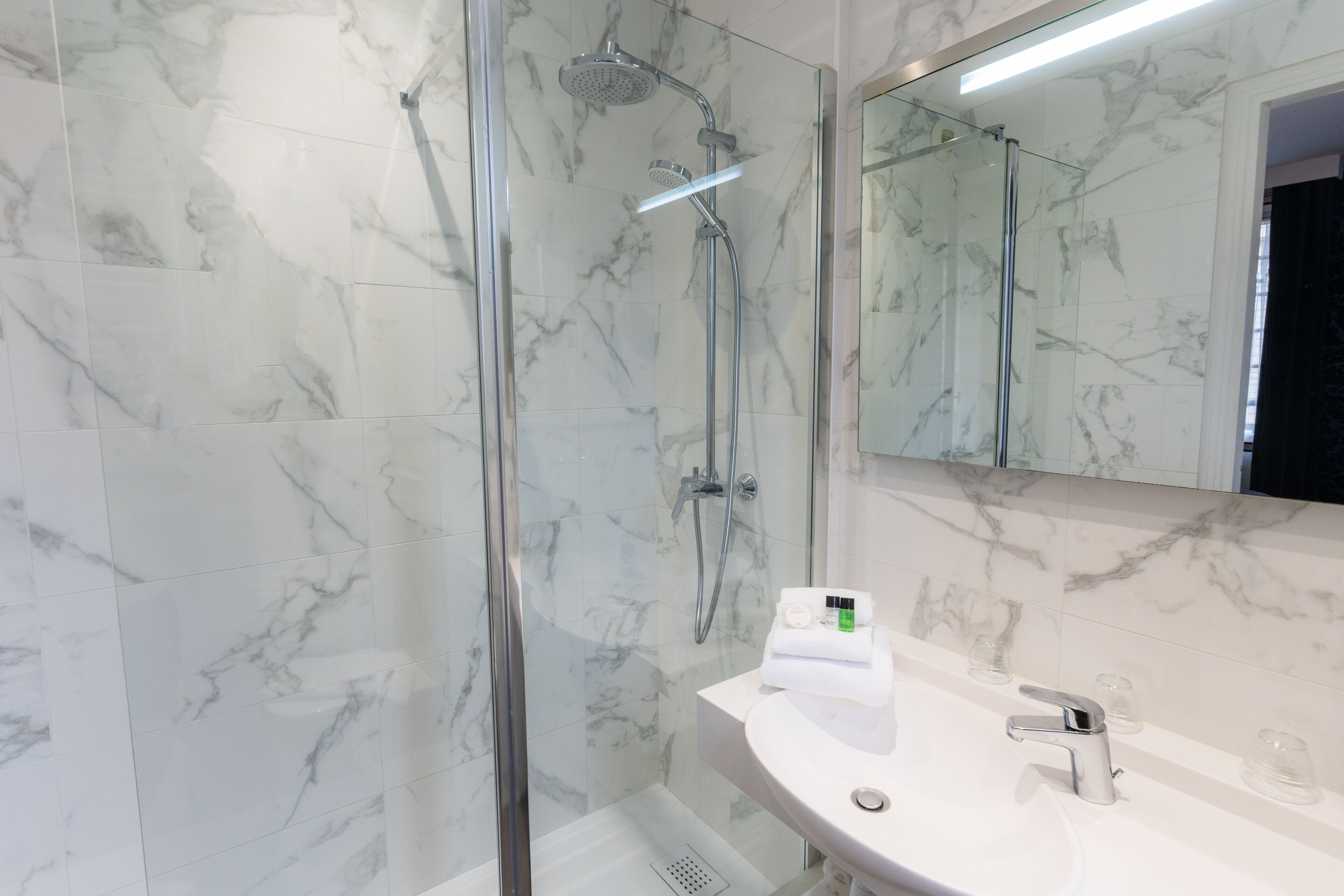 A modern bathroom with a glass-enclosed shower, a marble-tiled wall, and a white sink with a mirror above it.