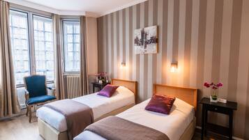 A hotel room with two beds, a chair, a nightstand, and a wall-mounted artwork.