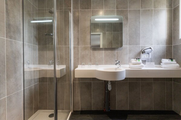 A modern bathroom with a glass shower enclosure, a white sink, and a mirror.