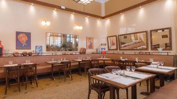 Een restaurant met meerdere tafels en stoelen, een bar en een grote spiegel aan de muur.