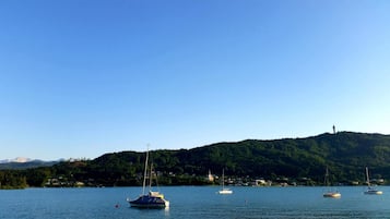 A calm lake with several sailboats anchored. A forested hill with a tower is visible in the background.
