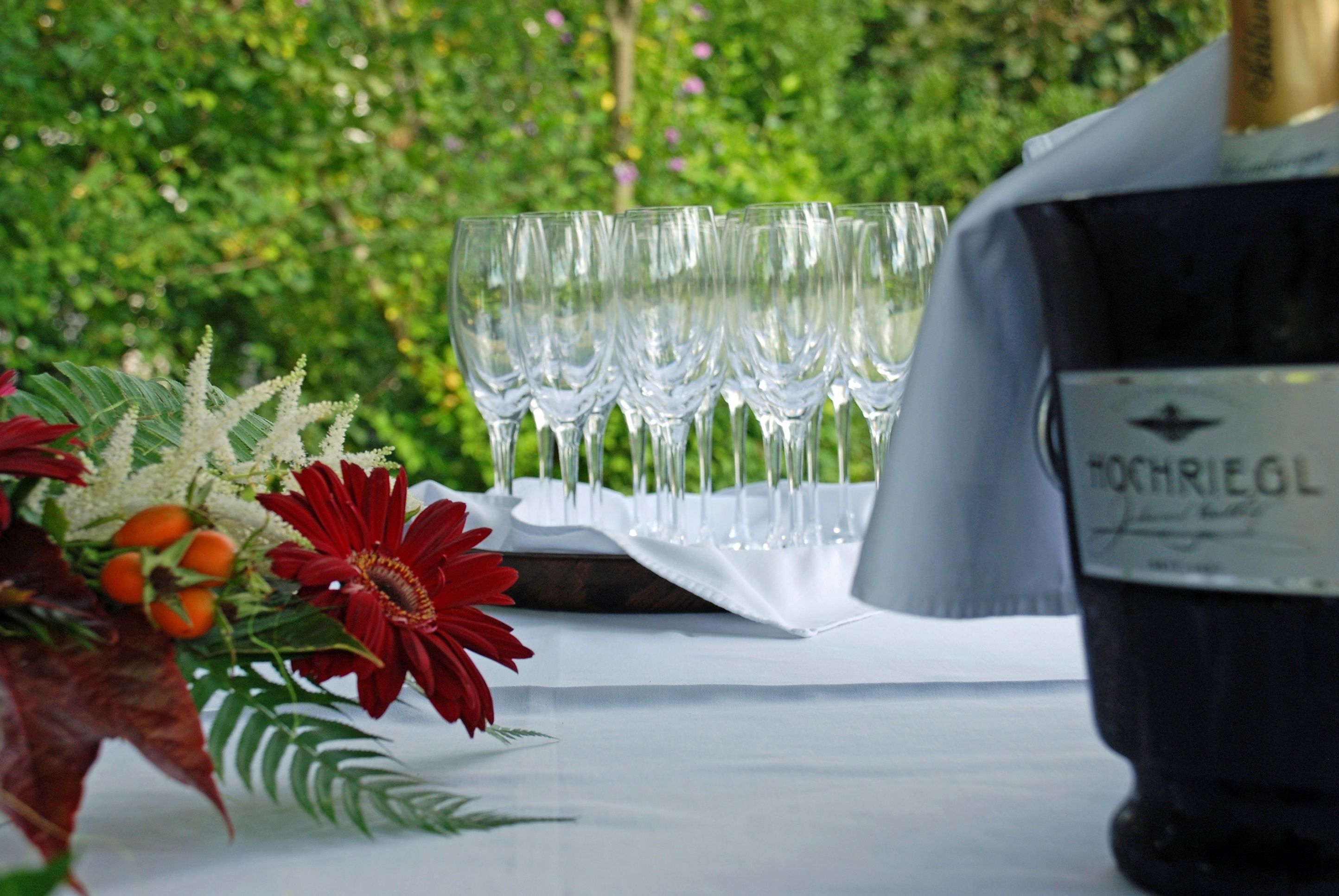 Una mesa con una botella de vino, copas y un arreglo floral.