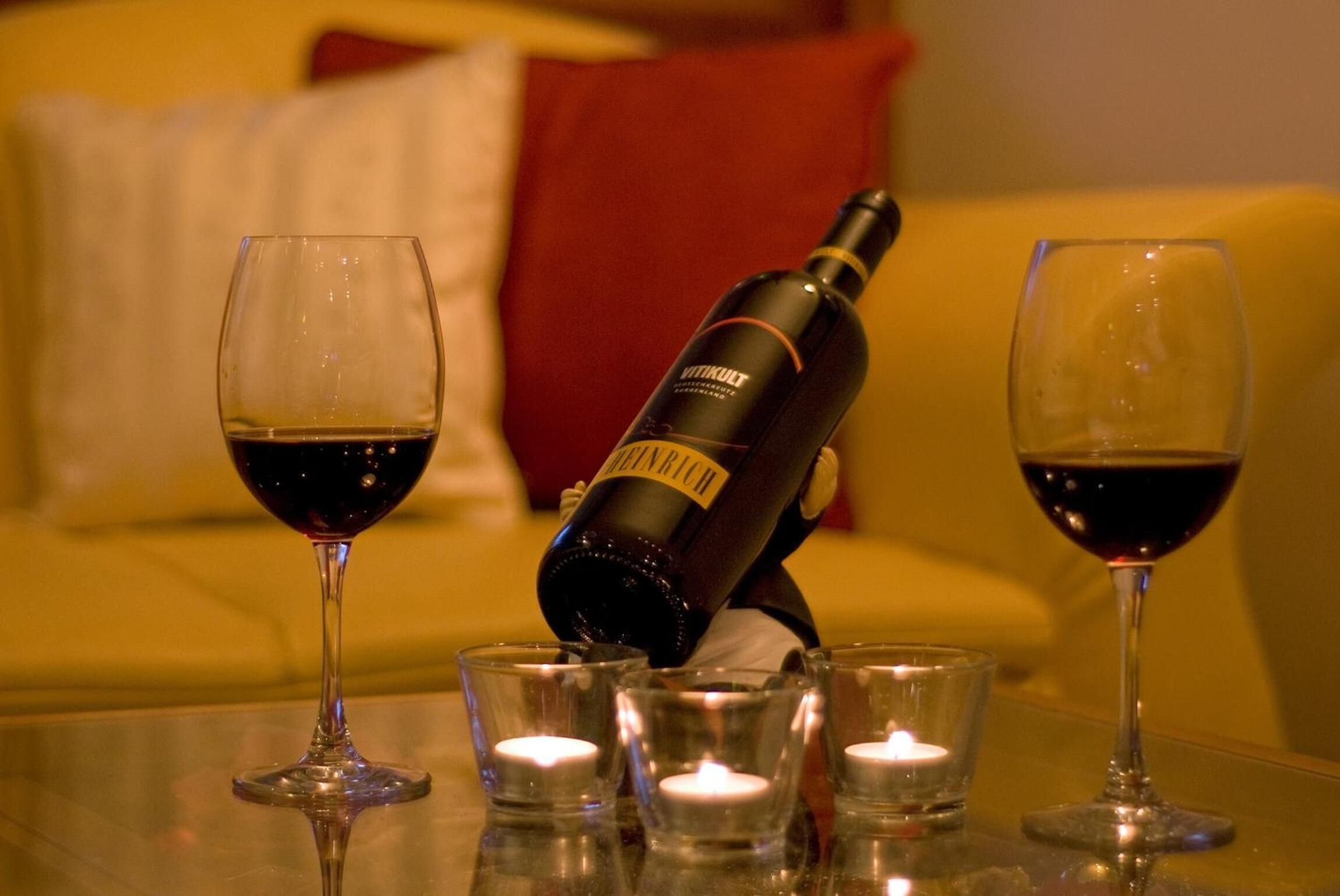 A bottle of wine, two glasses, and four shot glasses on a table with candles.