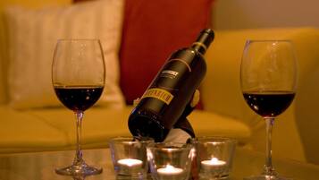 A bottle of wine, two glasses, and four shot glasses on a table with candles.