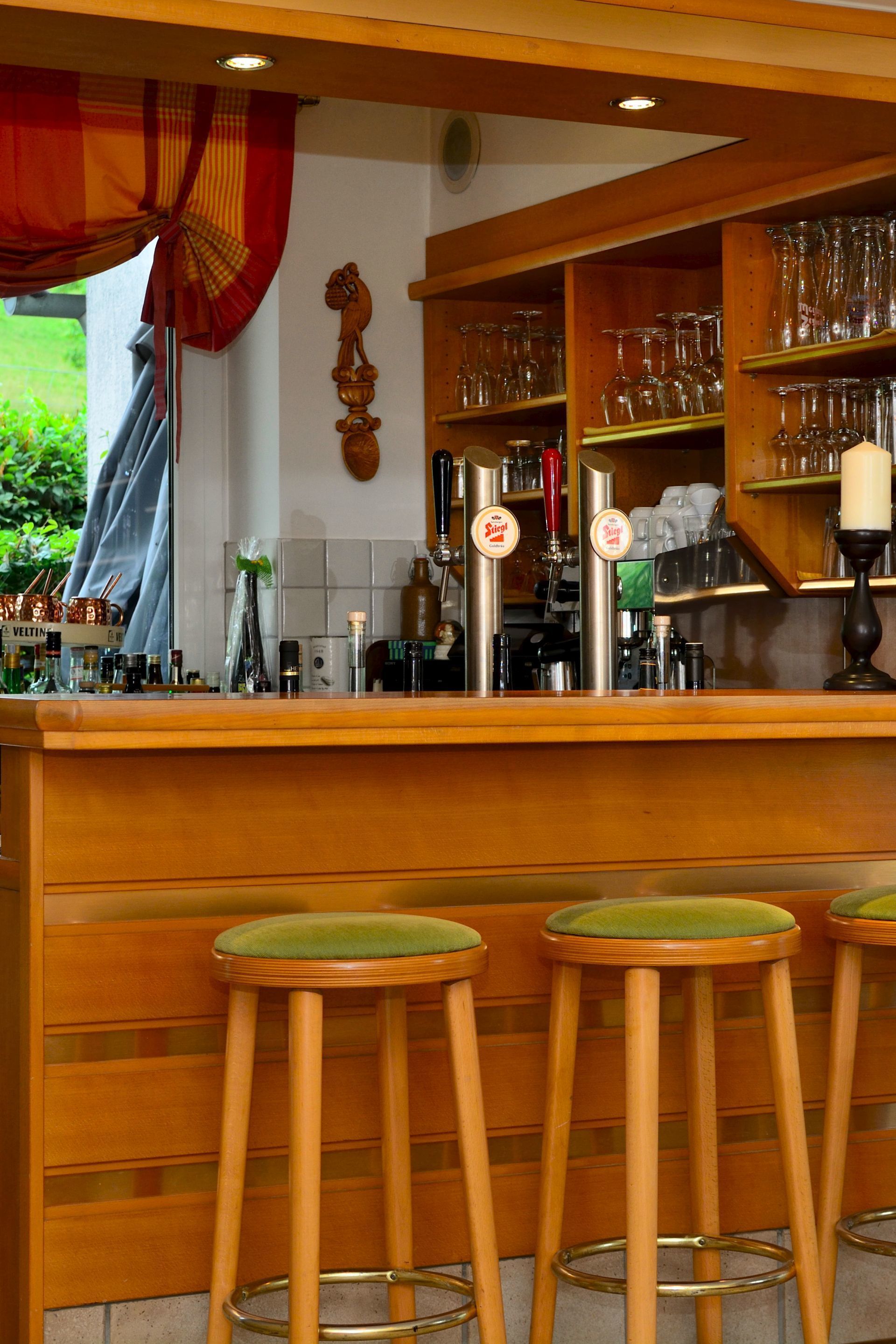 Un espace bar avec des tabourets en bois, un comptoir avec des robinets et des étagères remplies de verres.