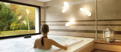 A spa room with a large window, a hot tub, and a wooden floor.