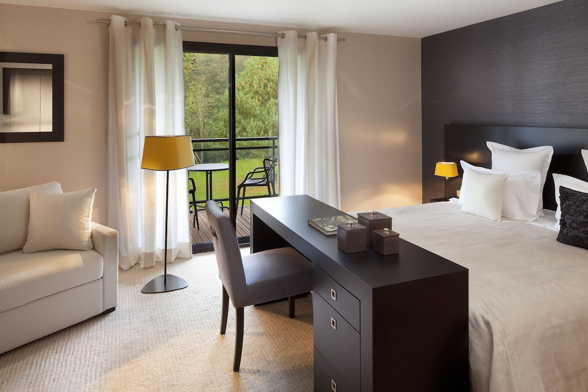 A modern hotel room with a bed, a desk, a chair, and a view of the outdoors.