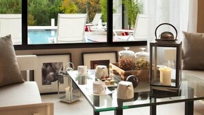 Ein modernes Wohnzimmer mit einem Glastisch, weißen Sofas, Blick auf einen Pool und einem großen Fenster.