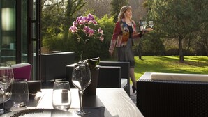 Ein Esstisch ist gedeckt mit Tellern, Gläsern und Besteck, mit einer Topf-Orchidee und einer Weinflasche darauf.