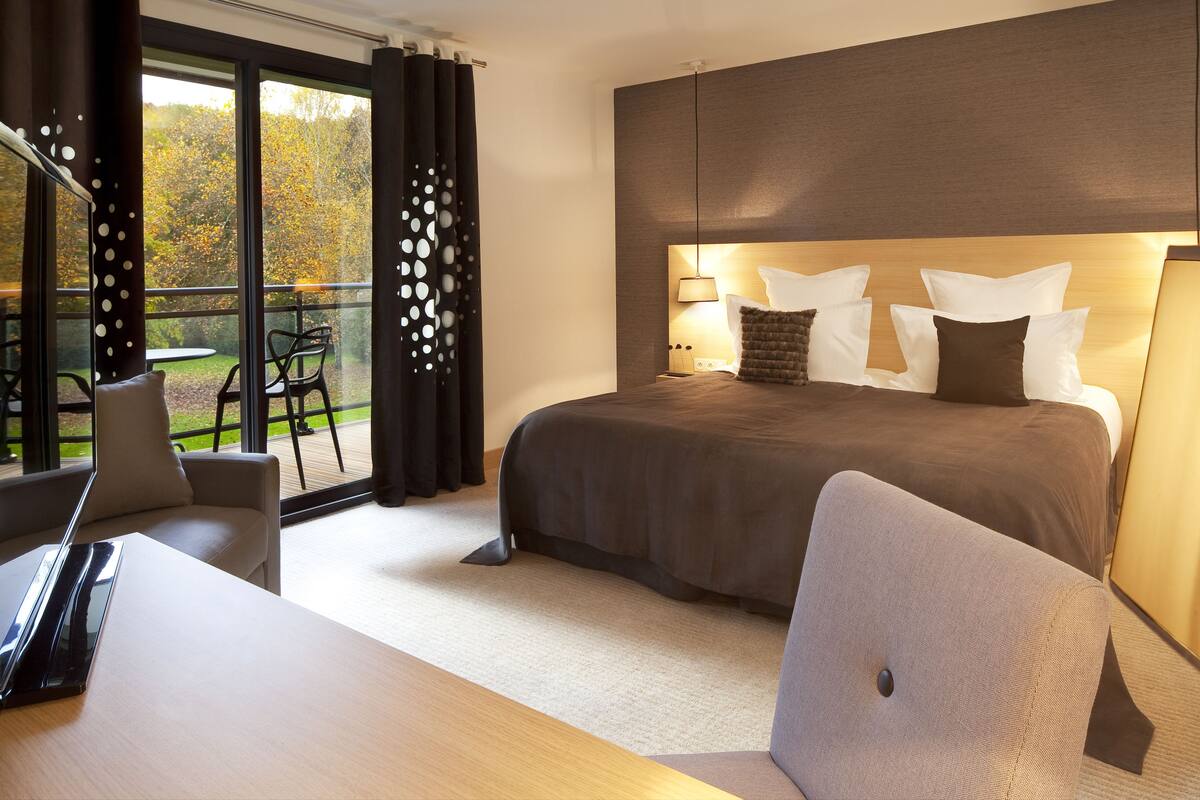 A modern hotel room with a large bed, a desk, and a view of the outdoors.