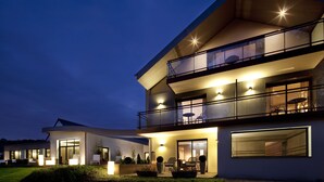 Ein modernes, zweistöckiges Haus mit Balkon, großen Fenstern und Sitzgelegenheit im Freien.